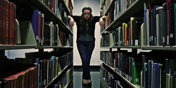 A student stands in between the bookshelves of a library